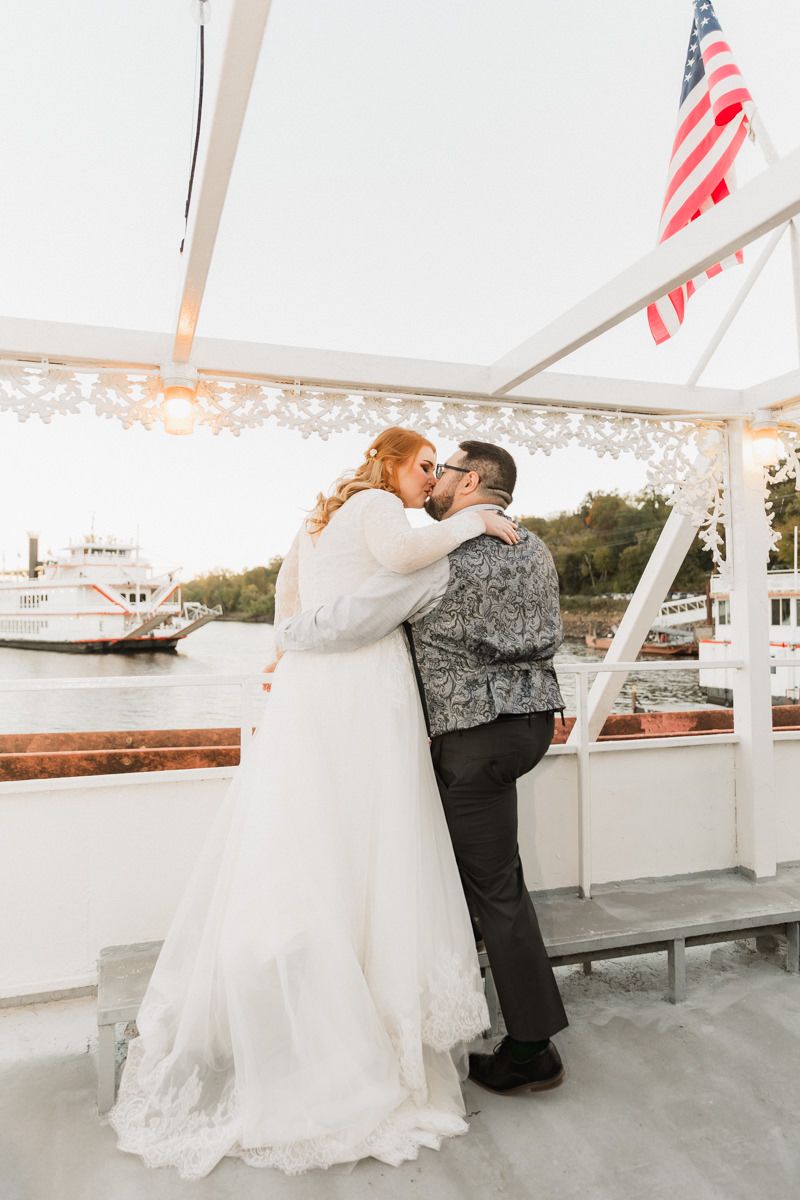 A romantic wedding moment on a white boat deck with American flags waving in the background.