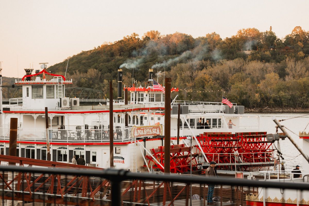 A panoramic view of a riverboat dock with historic paddle wheelers moored along a waterfront at sunset.