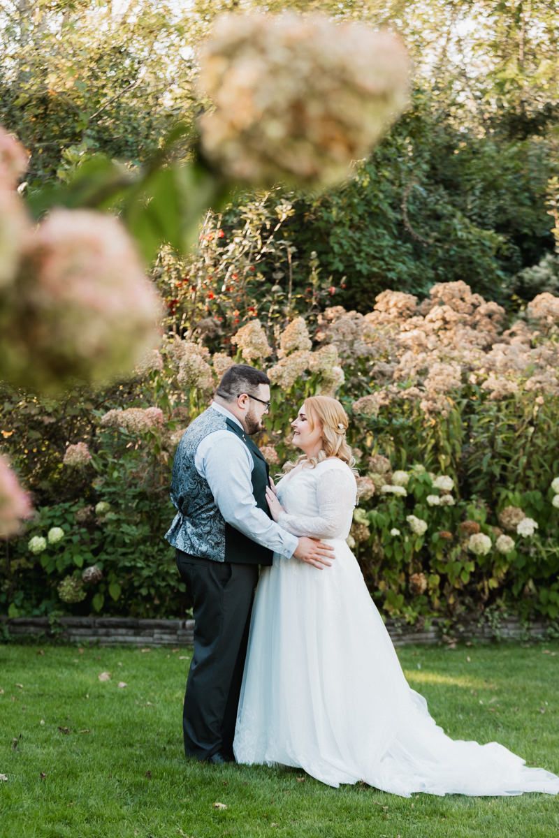 Romantic wedding couple embraces in a lush garden setting with blooming flowers during golden hour.