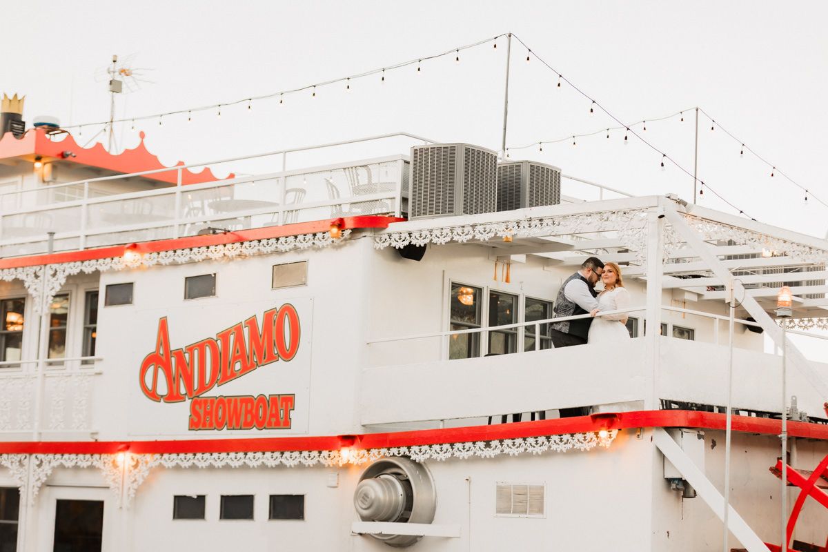 Top deck of white riverboat with red trim and string lights under bright sky.