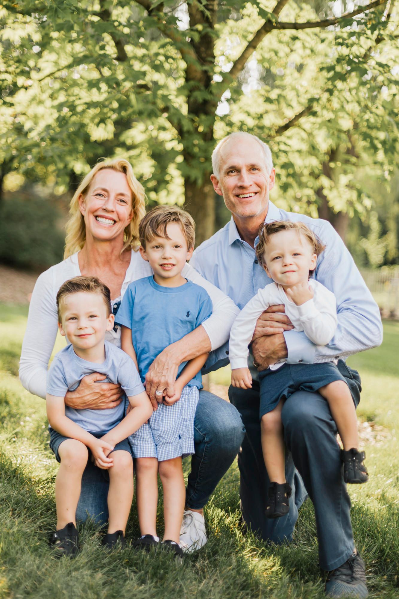 Family group sitting together on grass during golden hour with natural lighting and trees.
