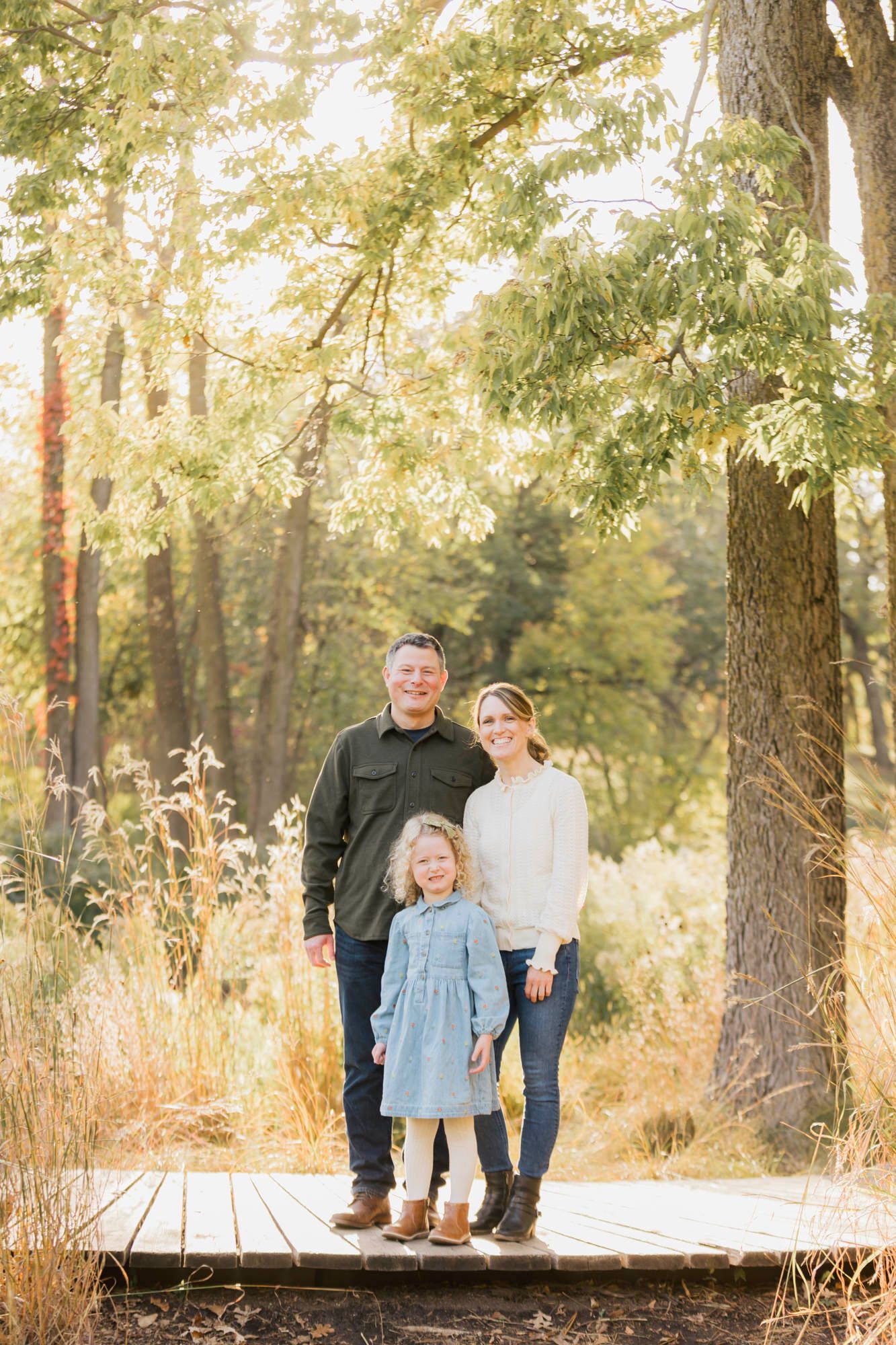 A family standing together on a wooden bridge surrounded by autumn foliage and trees.