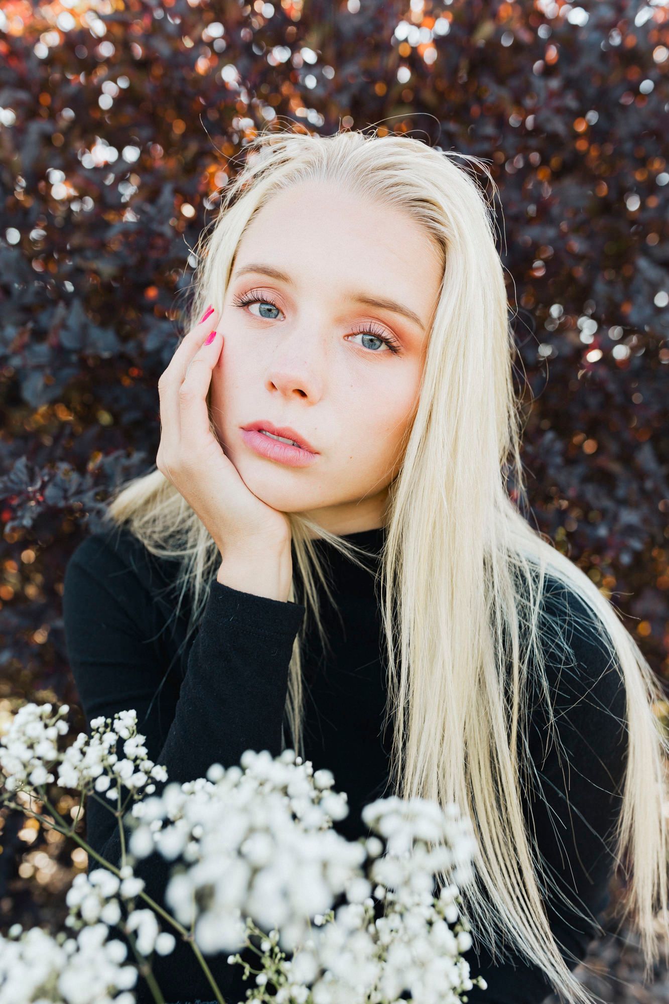 Artistic portrait with blonde hair against dark foliage with white flowers in foreground.