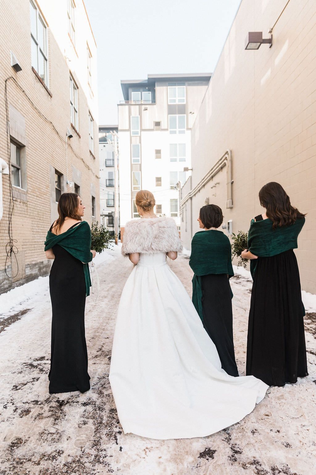 A group wearing emerald green dresses and a bride in white posing against a snowy backdrop.