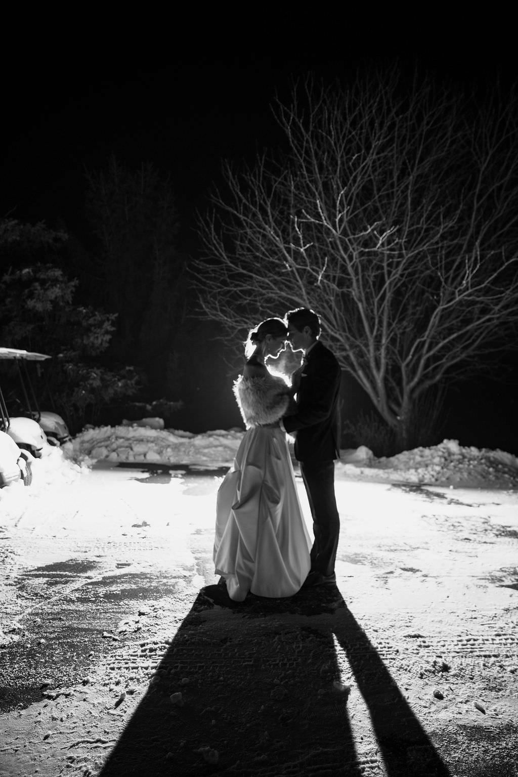 Artistic black and white winter wedding photo showing silhouettes in snow.