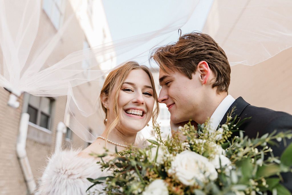 Wedding party poses together with elegant white draping and floral arrangements in a bright indoor space.