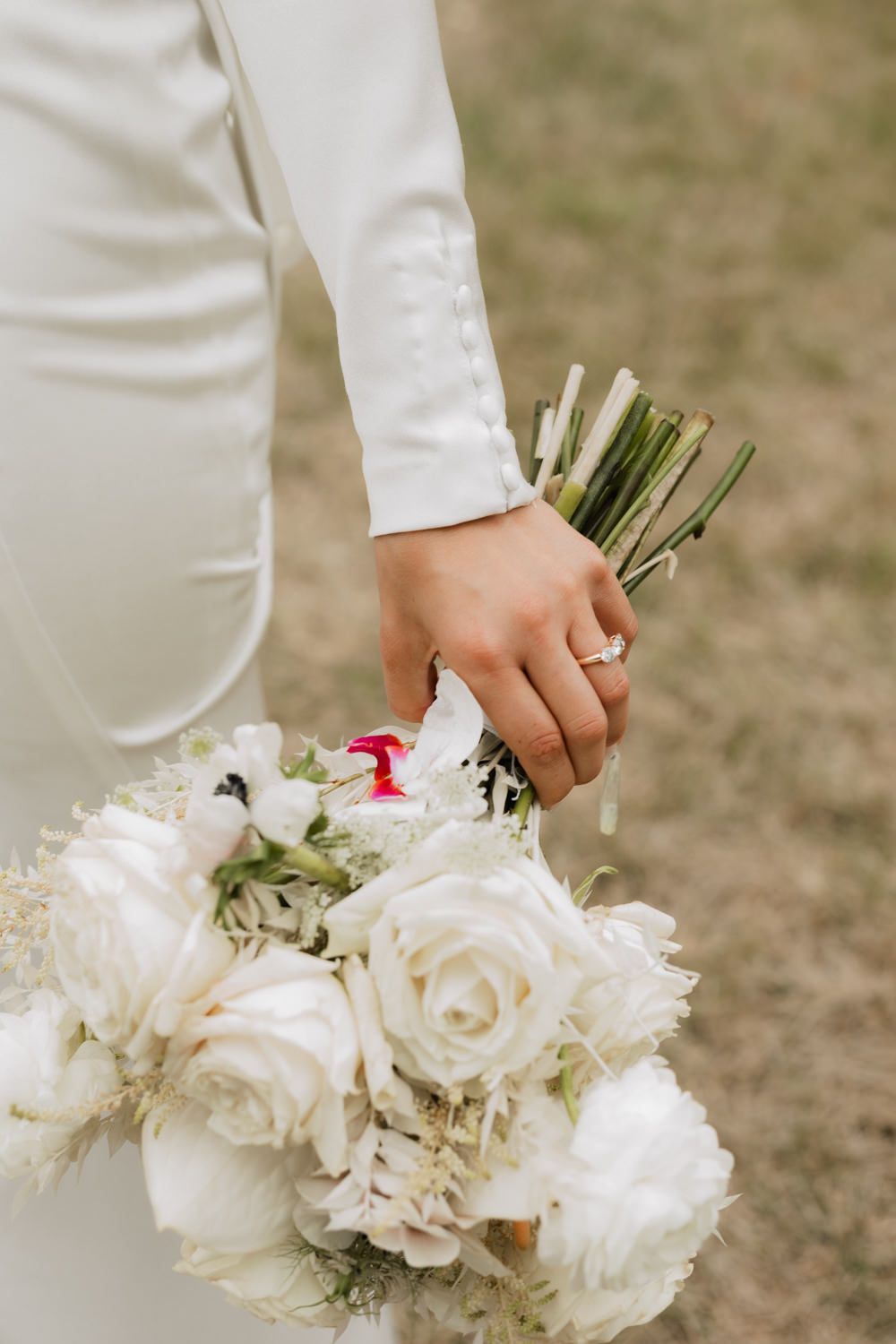 A white wedding bouquet with roses and delicate flowers being held against a natural outdoor background.