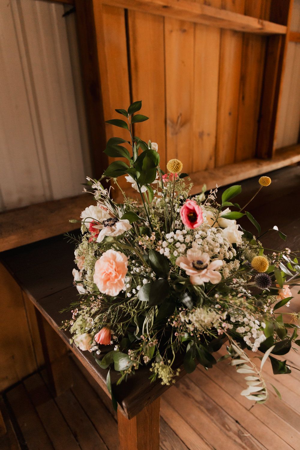 Wedding floral arrangement with pink and white flowers on rustic wooden surface with natural greenery accents.