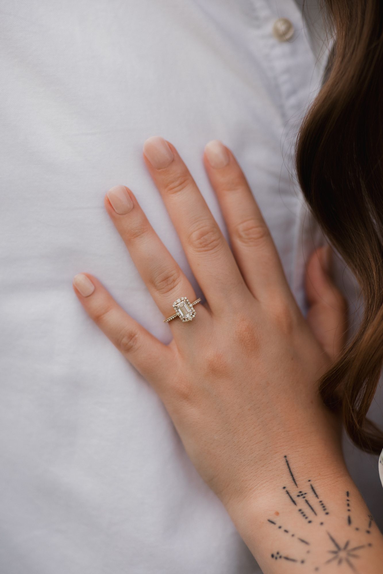 Close-up of a hand wearing an emerald-cut diamond engagement ring, with a delicate star tattoo on the wrist.