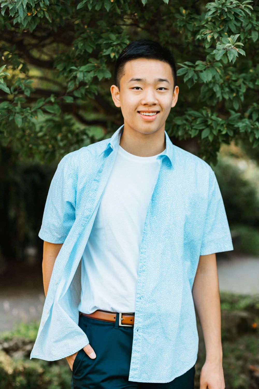 Lifestyle portrait showing a blue button-down shirt and white tee against garden foliage.