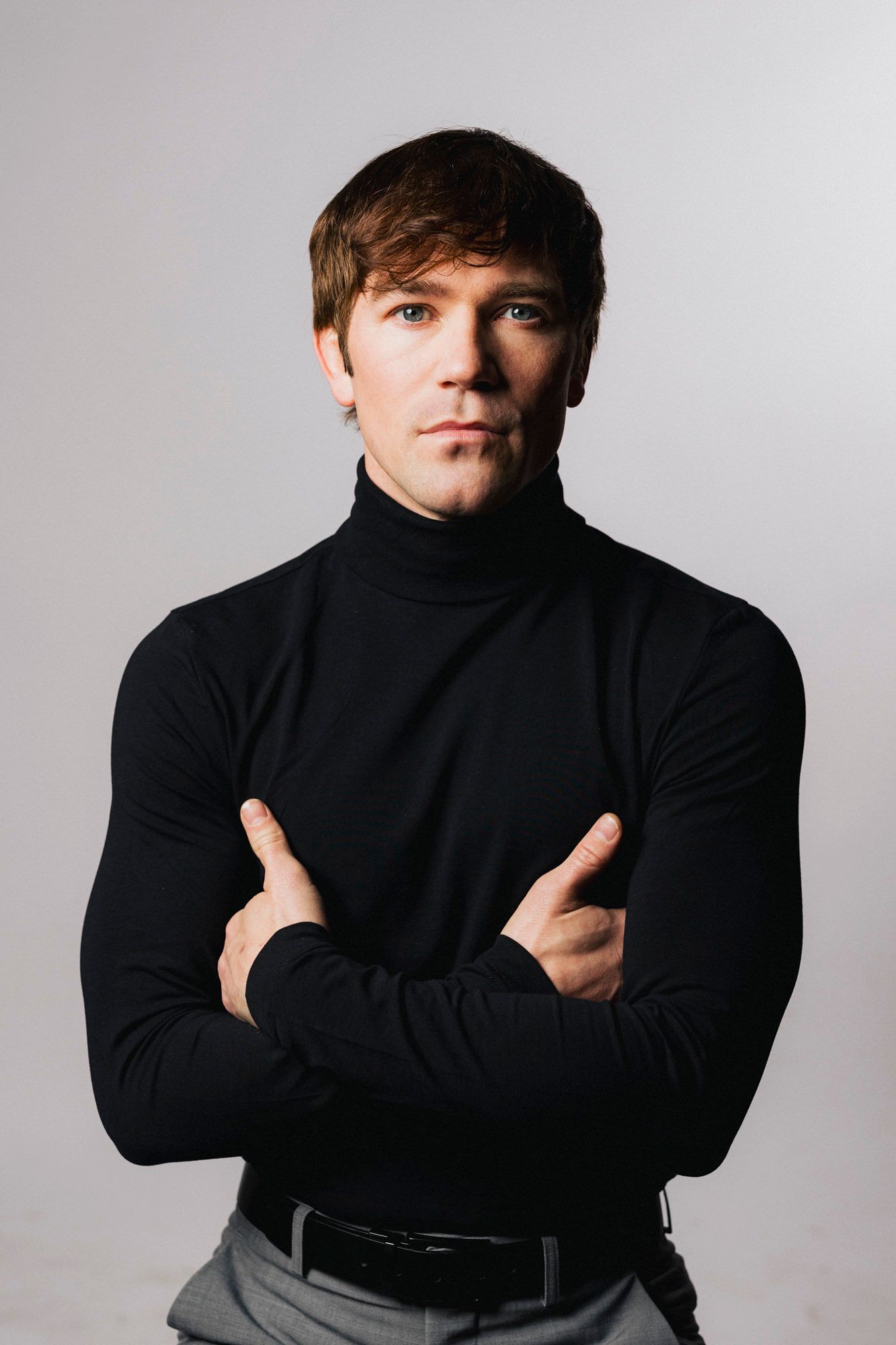 Professional studio portrait of person in black turtleneck sweater with crossed arms against light background.