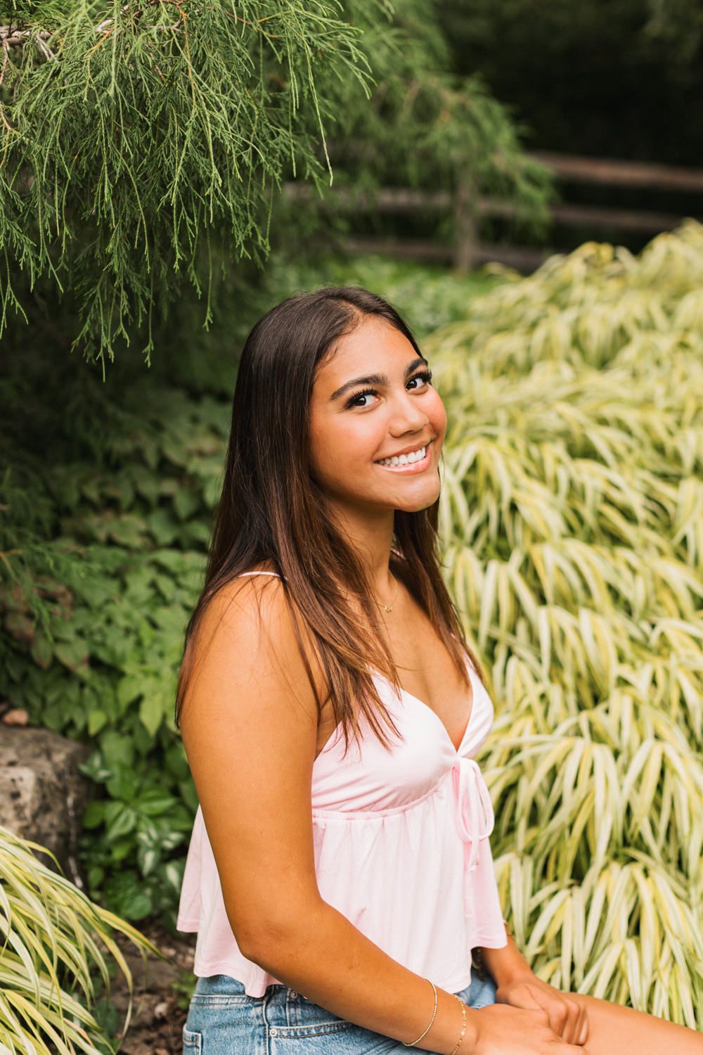 Summer portrait amongst lush greenery showcasing a pink top and denim shorts in a natural garden setting.