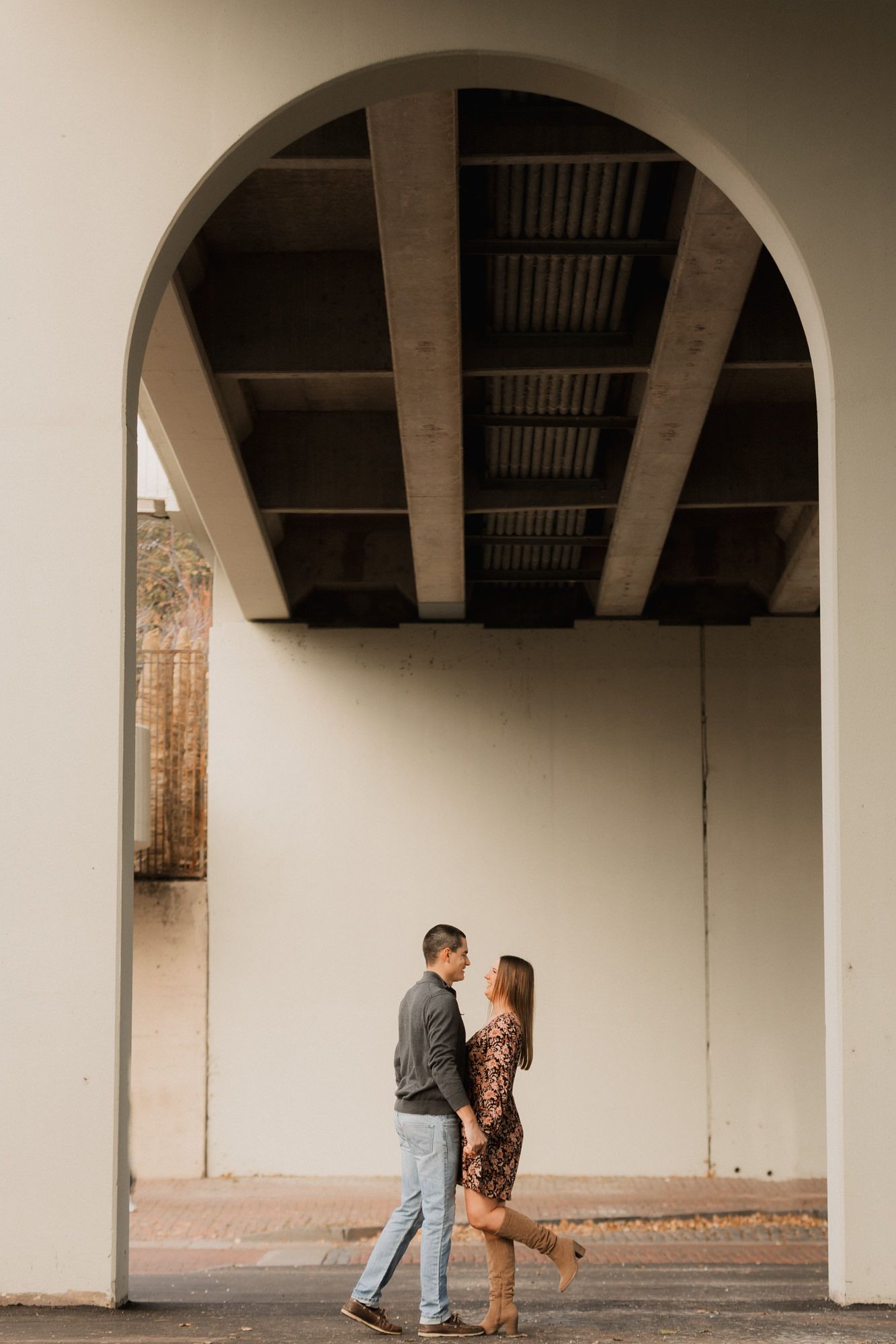 Couple sharing a tender moment under an arched bridge in soft natural light.