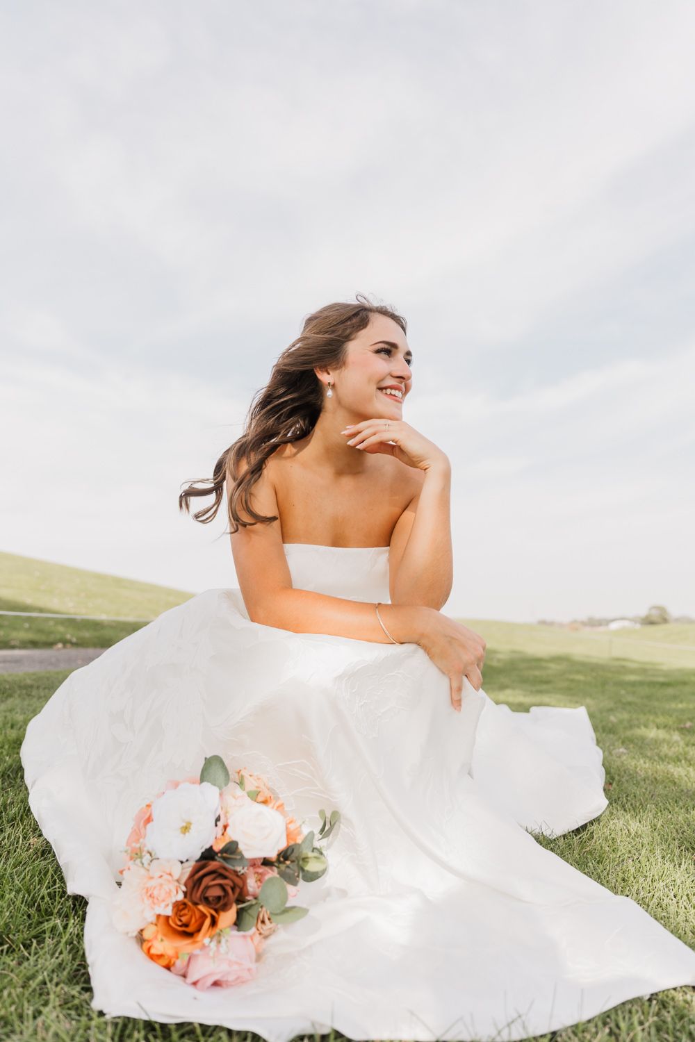 A bride in a flowing white dress twirls gracefully in a grassy field, her gown billowing in the breeze.