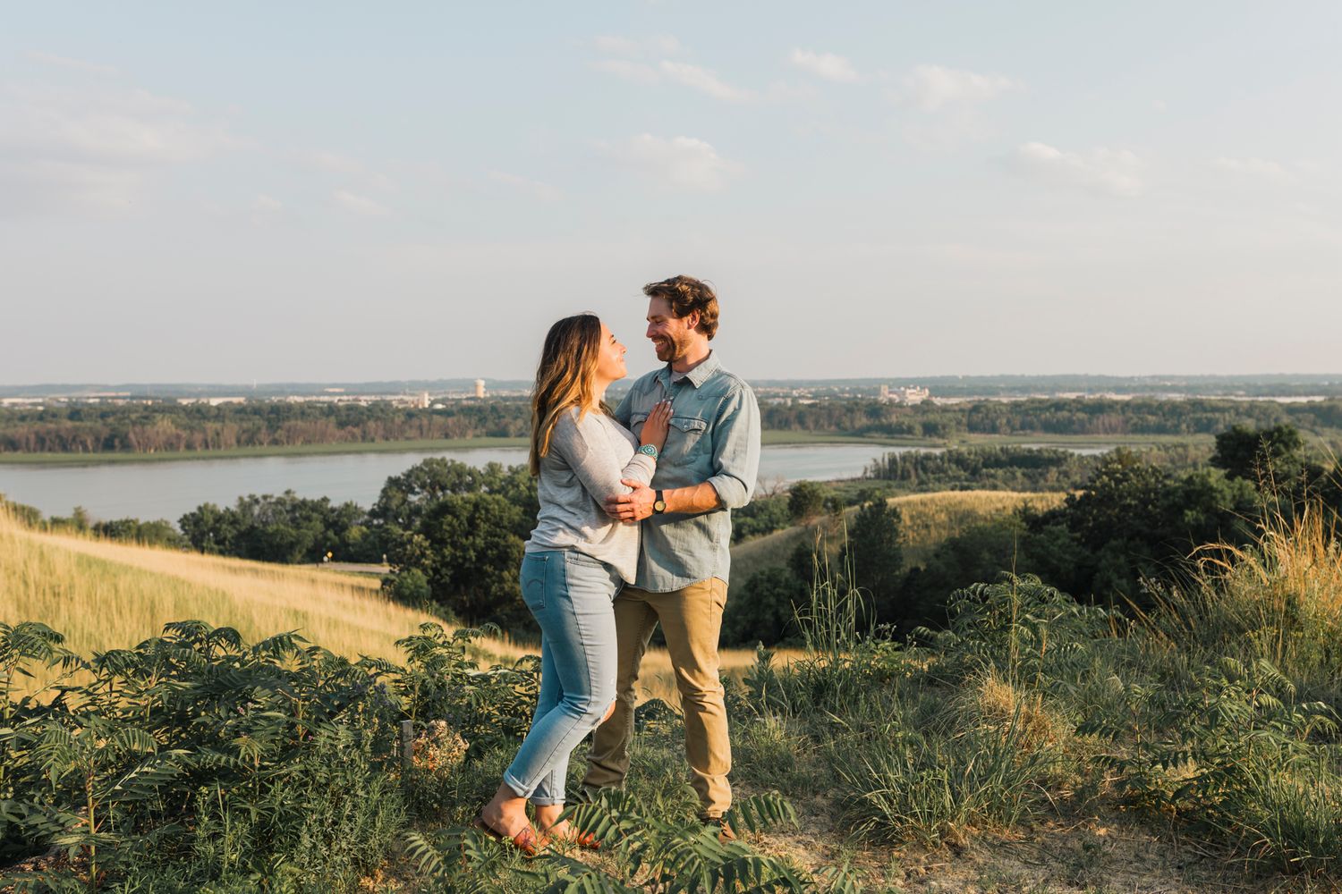 Couple embracing on hilltop overlooking scenic lake during golden hour.