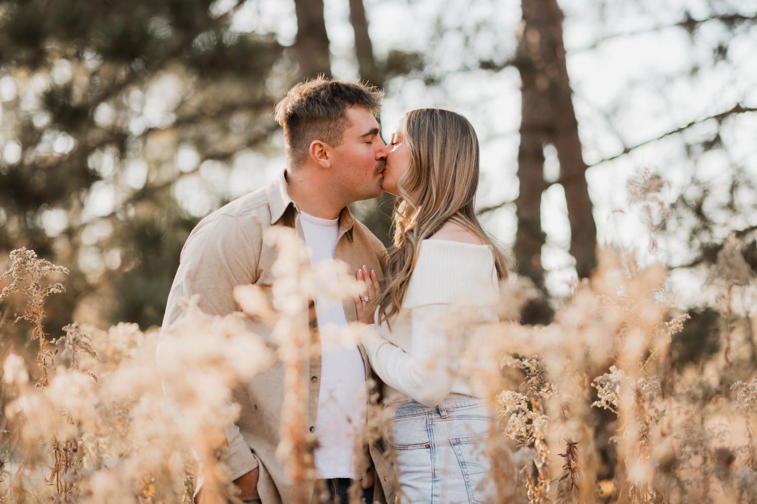 A couple sharing an intimate moment among tall grasses and trees during golden hour.