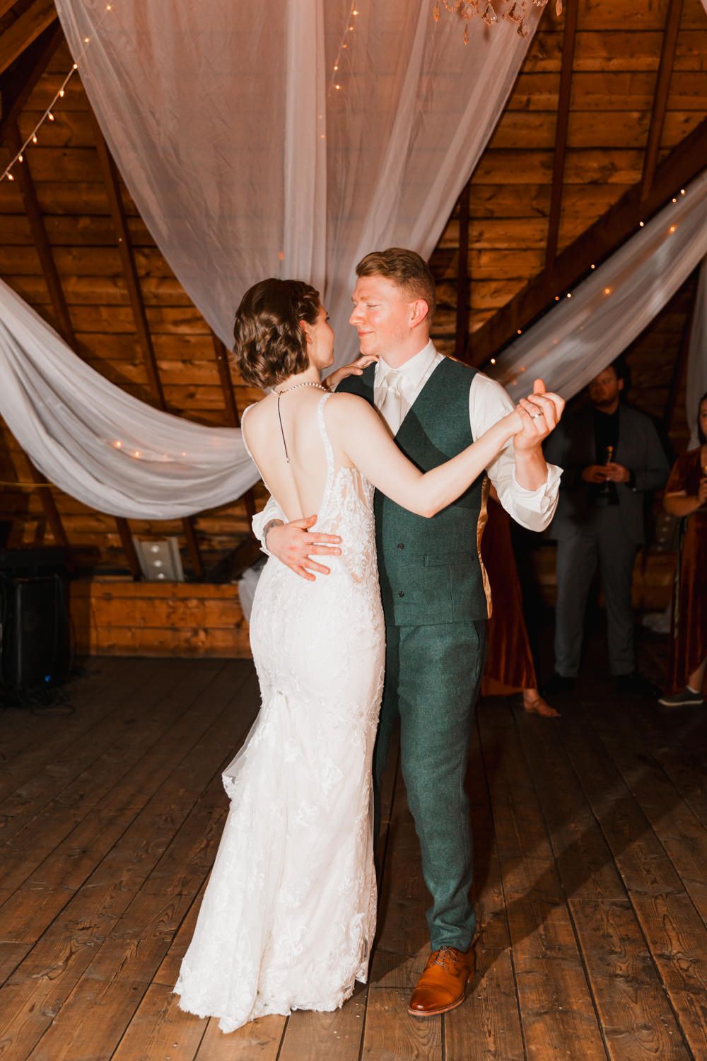Newlyweds share a romantic dance together in a rustic barn venue decorated with flowing white drapes.