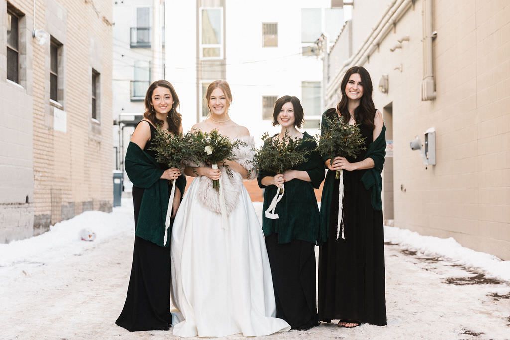 Wedding party poses together against neutral exterior walls wearing contrasting black and white formal attire.