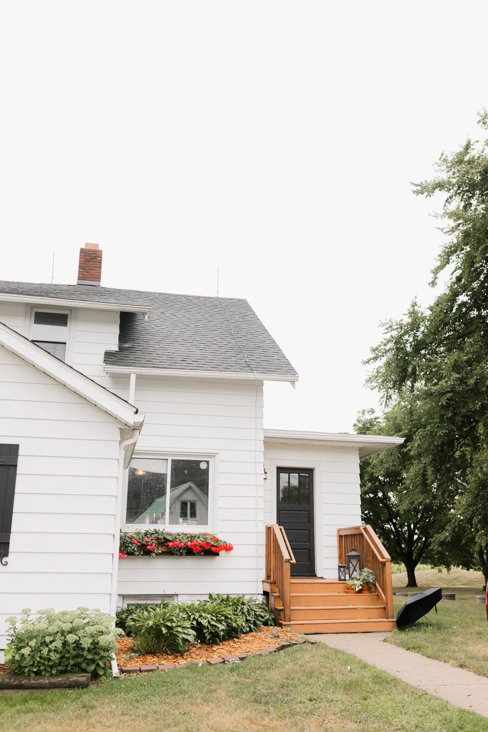 White farmhouse exterior with wooden deck stairs and red flower boxes under windows.