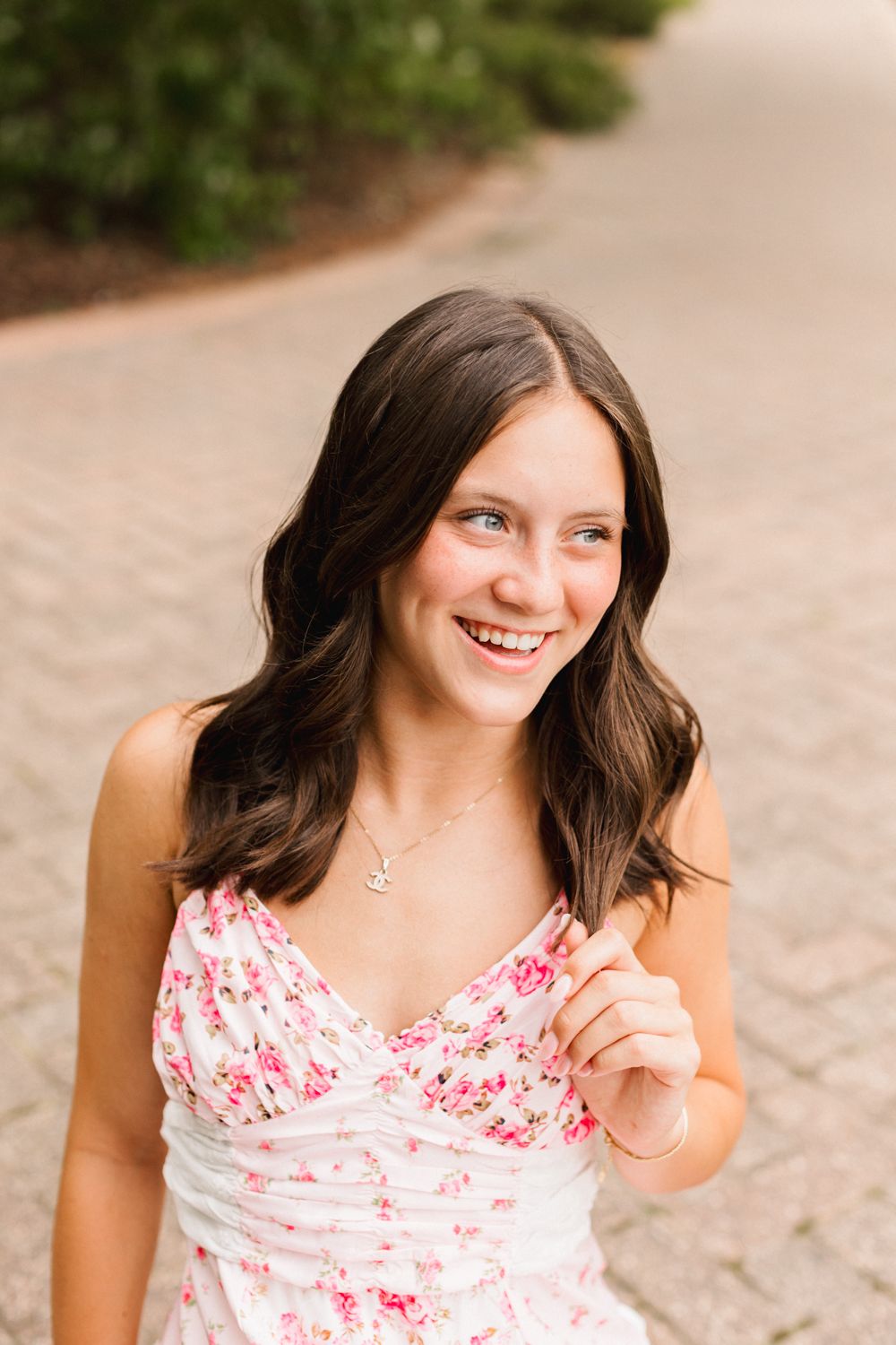 A portrait of someone in a pink and white floral dress smiling warmly against a natural outdoor background.