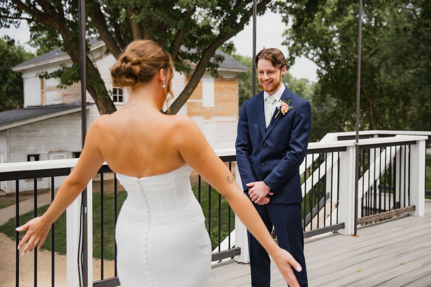 Bride in strapless white gown shares first look moment with groom in navy suit on outdoor deck.
