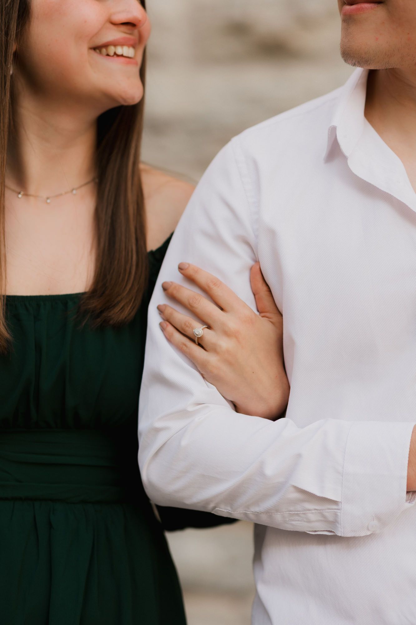Close-up of smiling woman in green dress holding mans arm showing engagement ring on her finger.