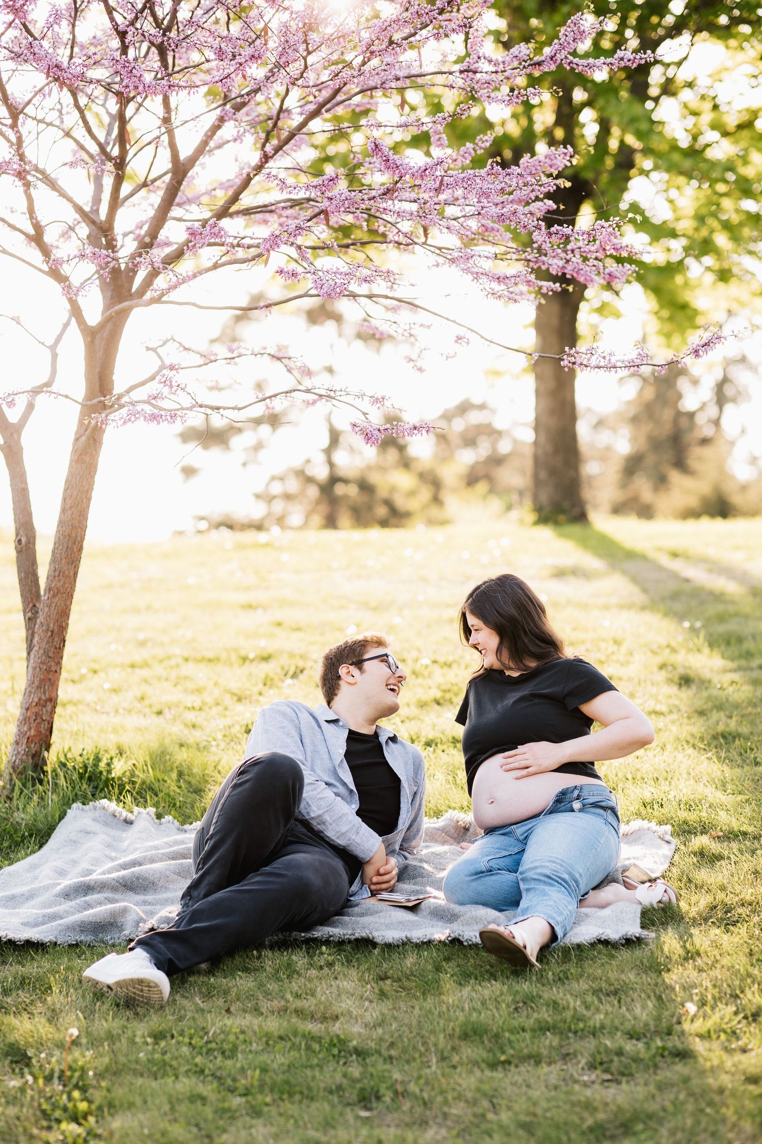Couple relaxes on blanket under blooming cherry blossom tree.