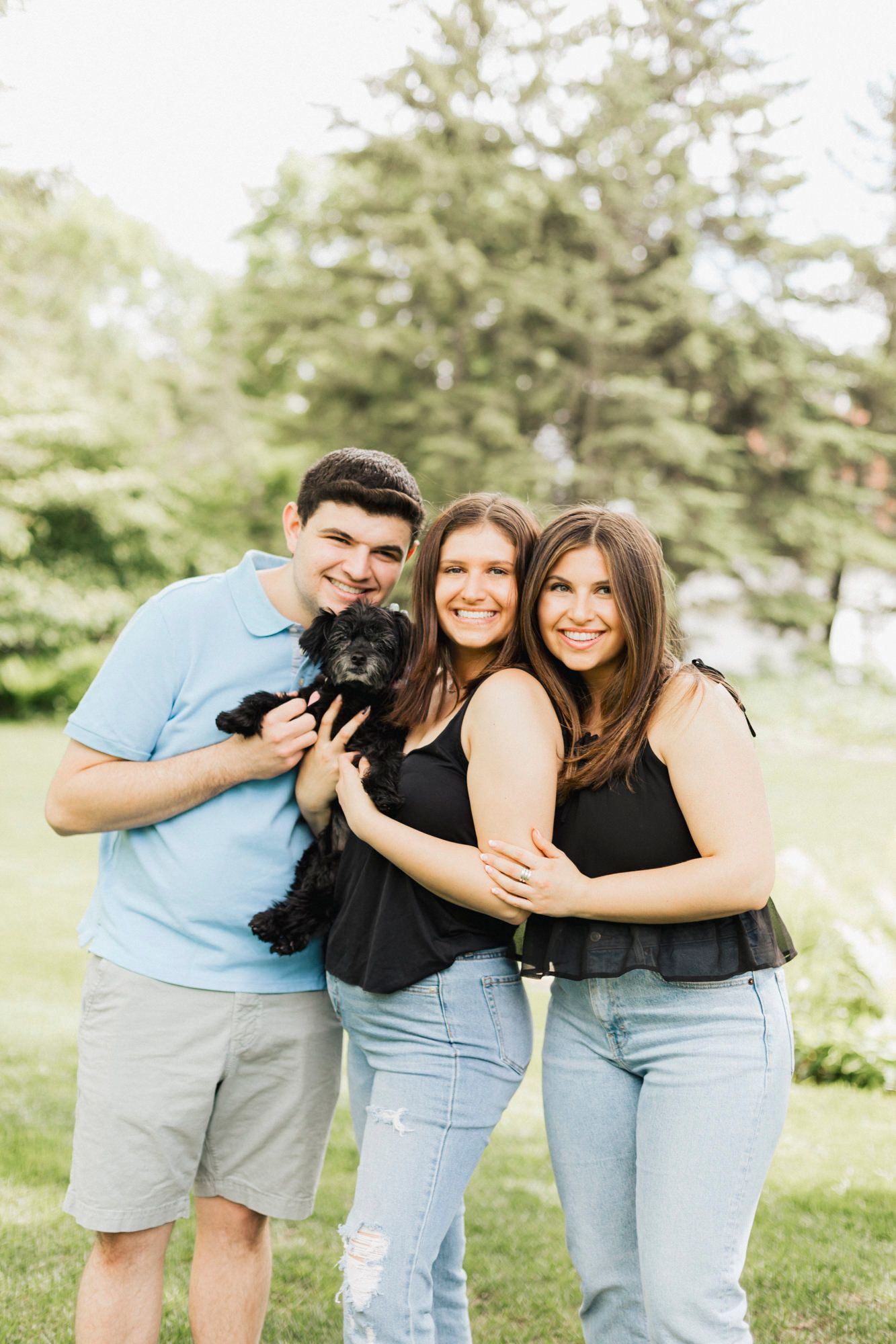 Three people and black dog pose together outdoors in casual summer attire.