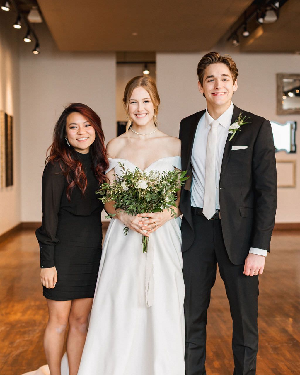 A wedding party poses in a rustic reception venue with hardwood floors and minimalist decor.
