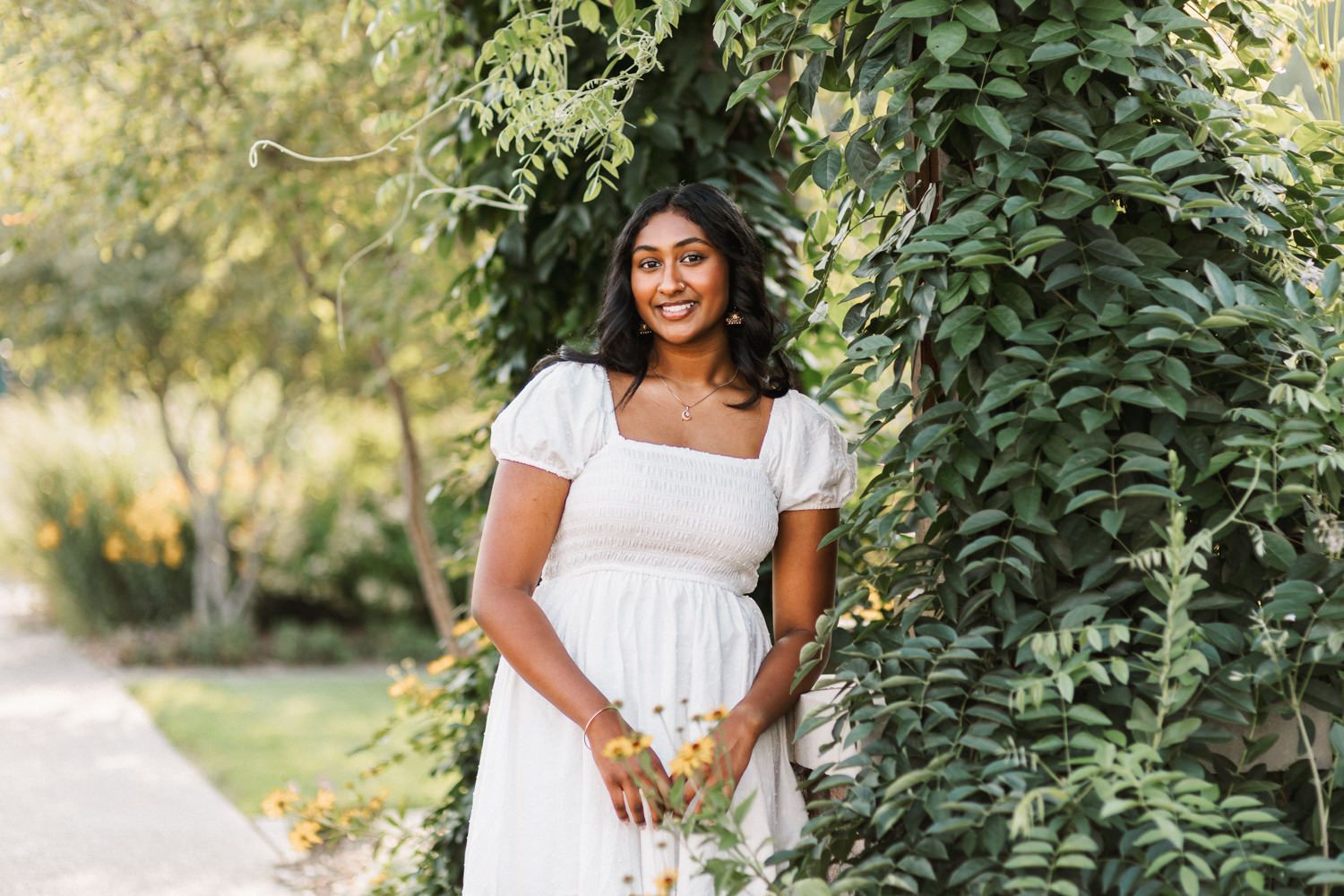 Casual portrait in white summer dress against lush garden foliage.