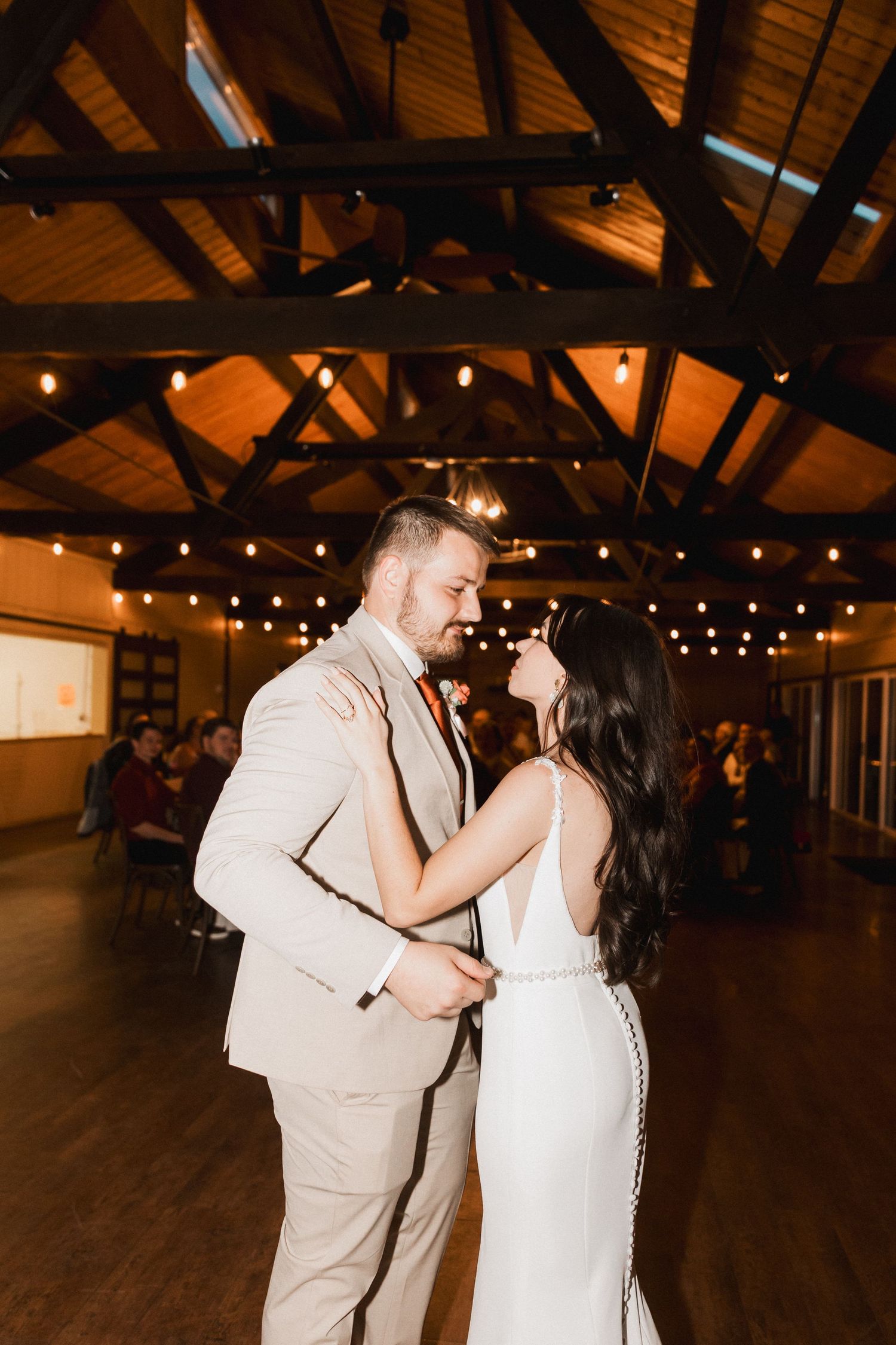 A couple shares their first dance in a rustic wooden barn venue illuminated by warm string lights.