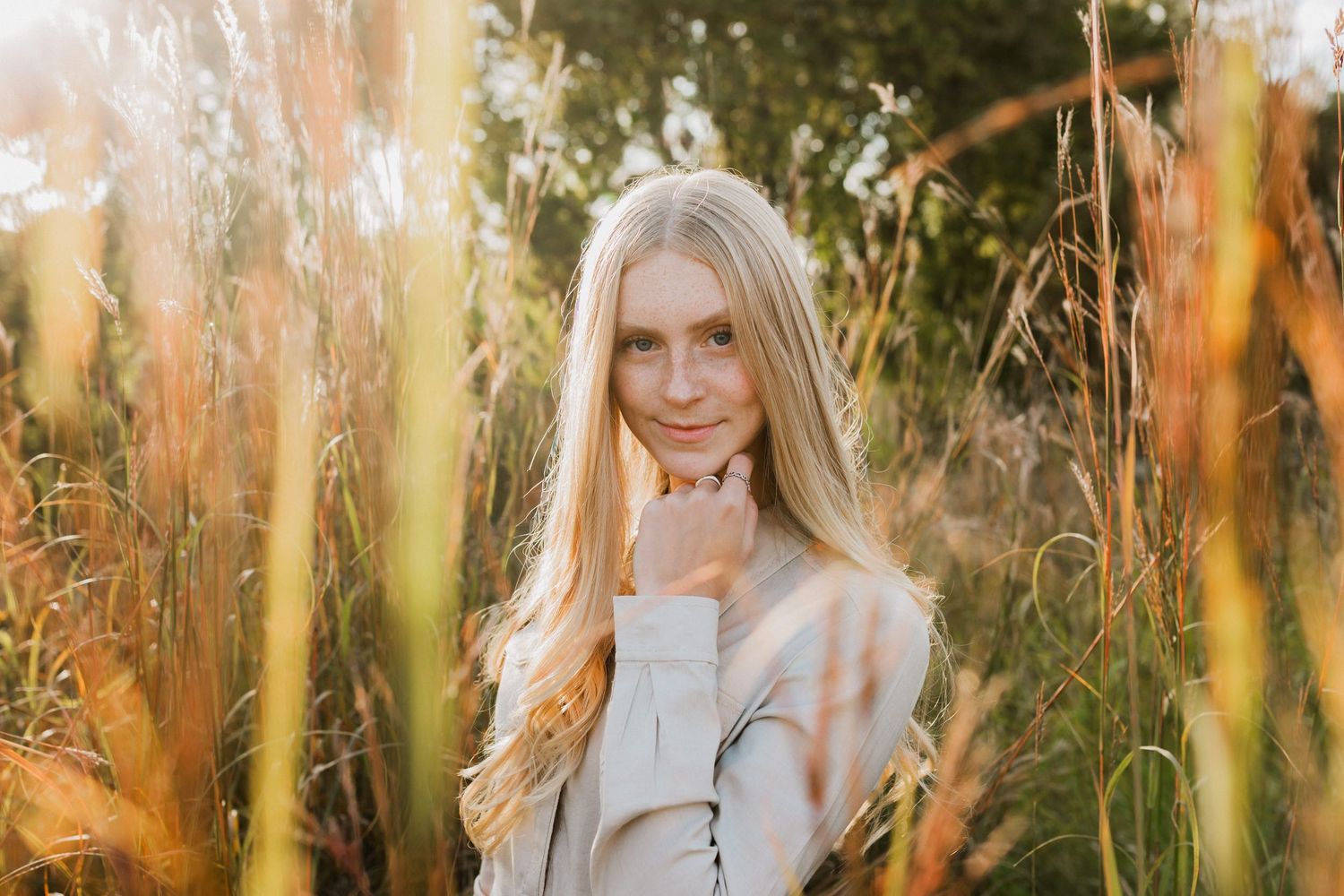 Woman in white dress poses in golden field of tall grass during sunset golden hour.