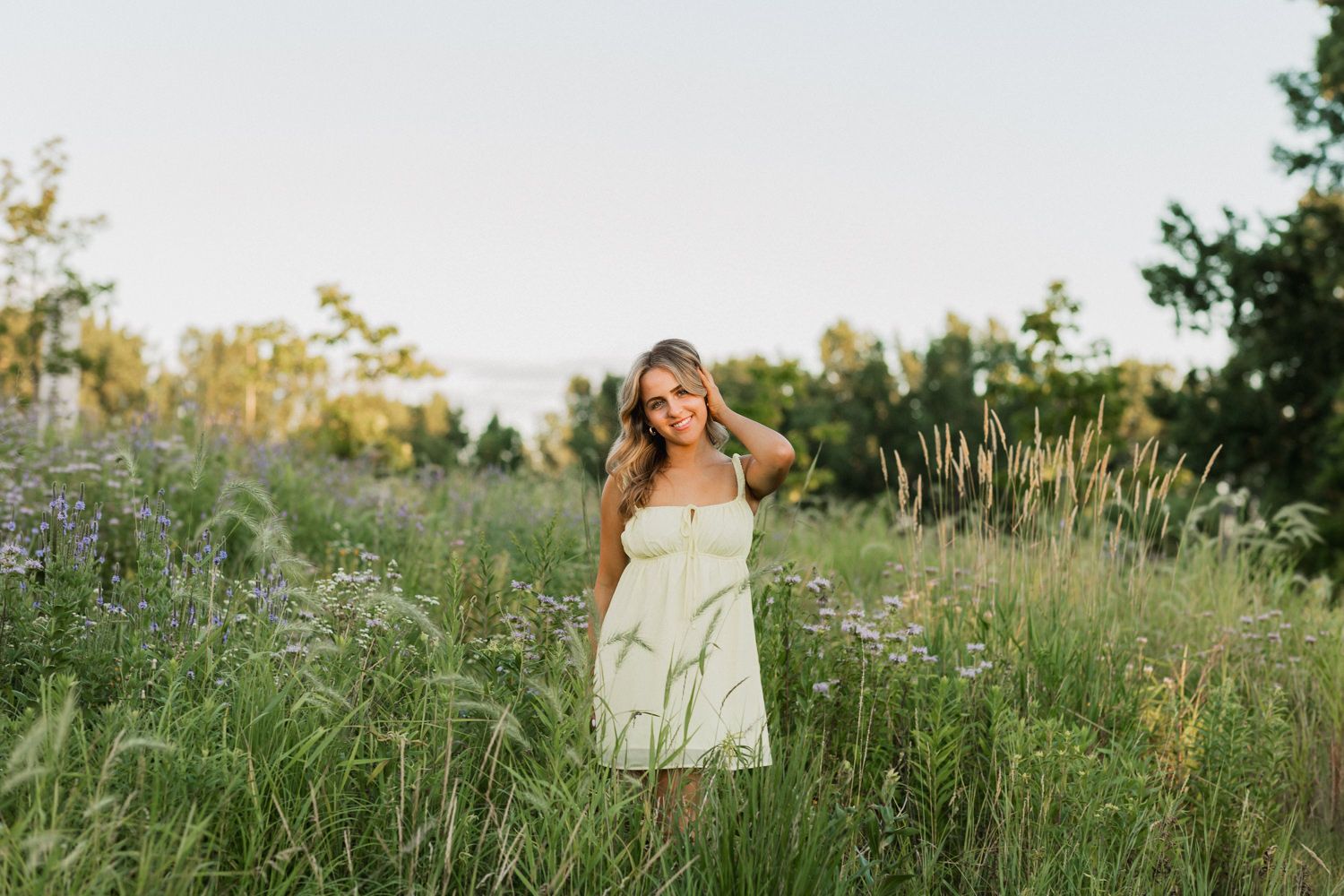 A person in a flowy white dress walks through a wildflower meadow during golden hour at sunset.