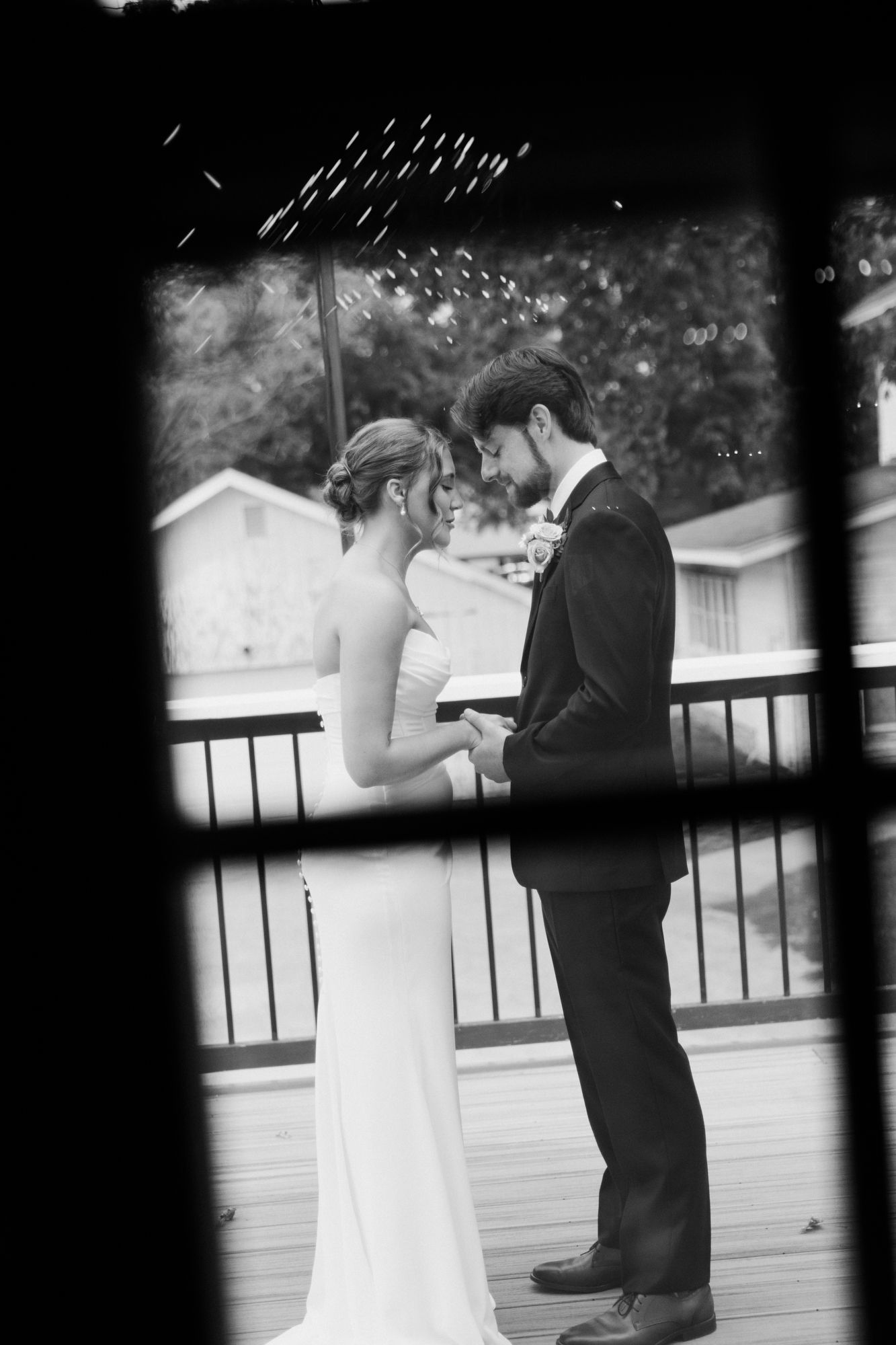 Black and white photo of bride and groom holding hands on a deck, sharing an intimate moment on their wedding day.