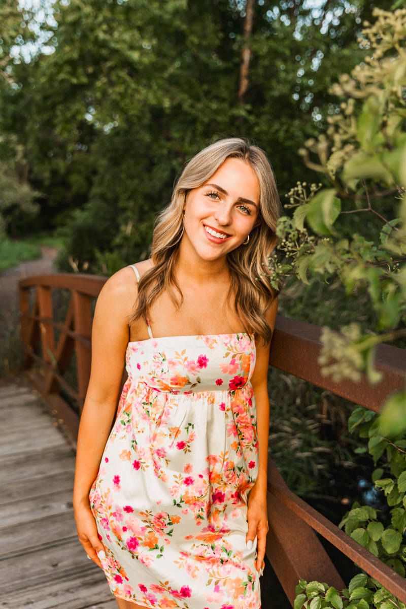 A floral summer dress in pink and white tones worn in an outdoor garden setting with greenery in the background.
