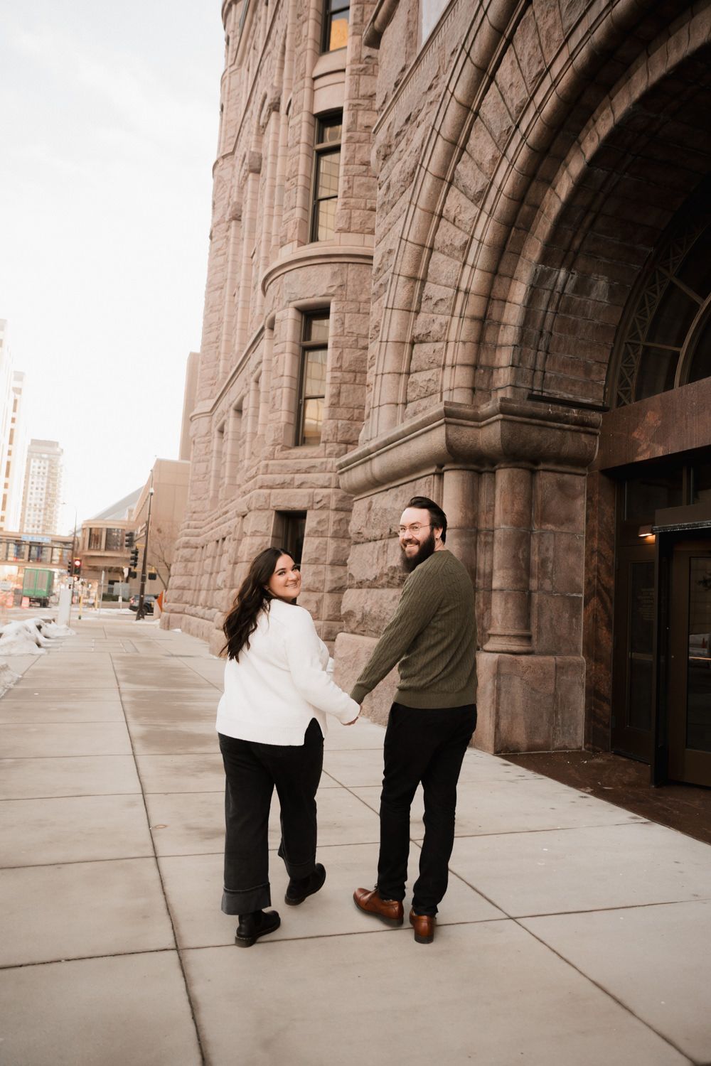 Two people walking and laughing together along a stone building's facade.