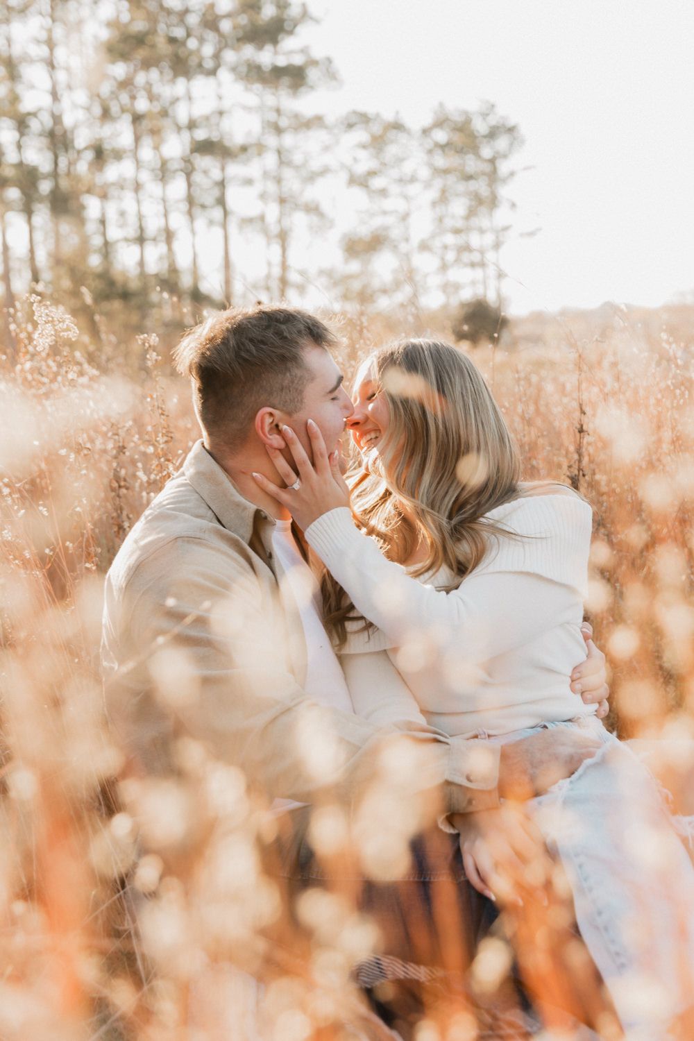 A romantic couple in white clothing shares intimate moments in a sunlit field of tall grass.