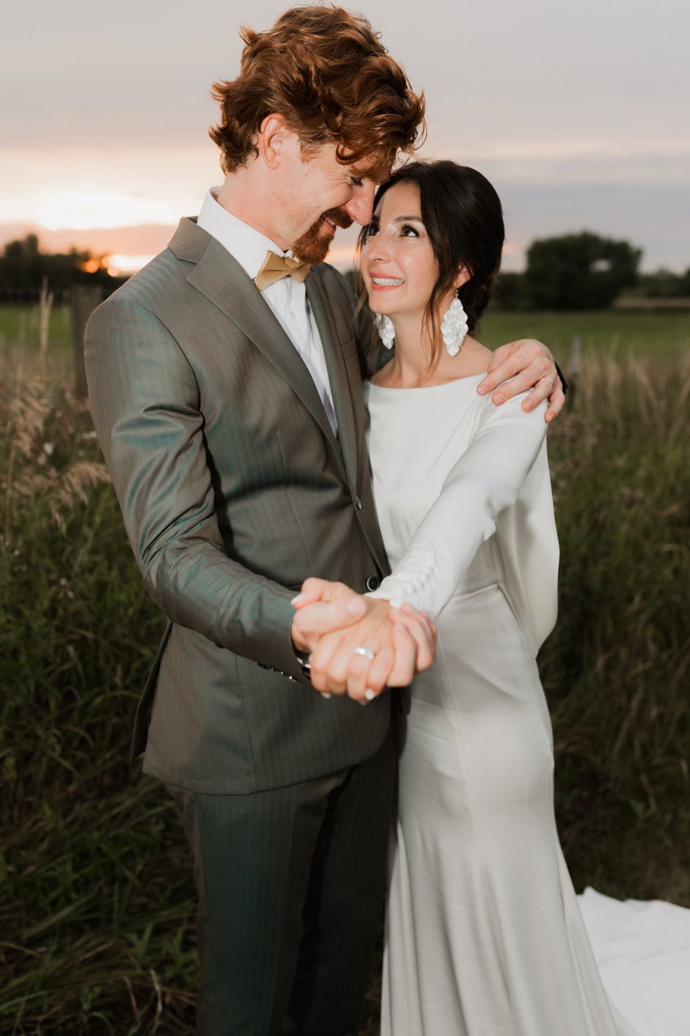 A romantic sunset portrait of newlyweds embracing in a field with golden hour lighting.
