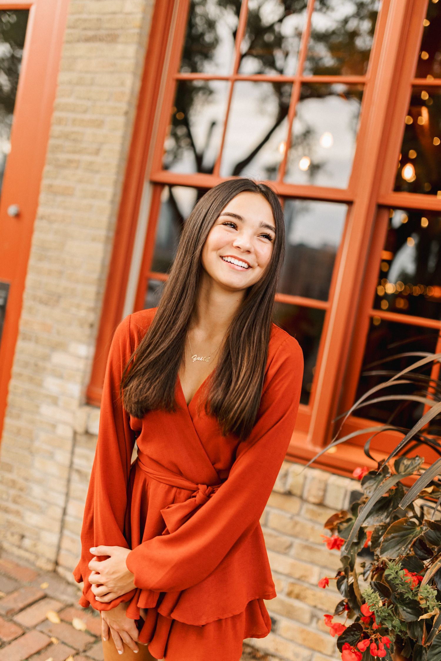 Portrait in red wrap dress standing by brick building with orange window frames.