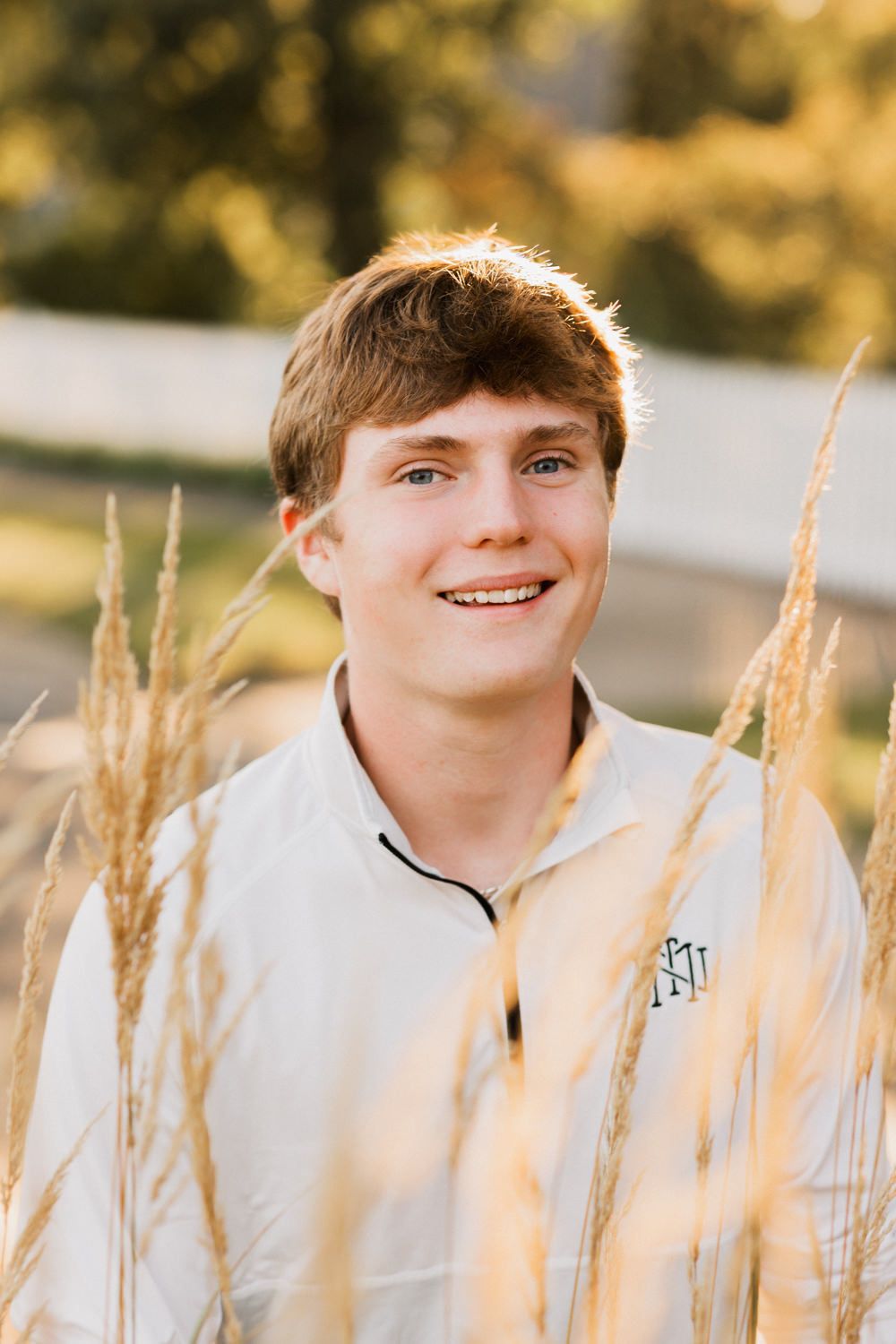 Portrait shot in golden light with tall wheat stalks framing the subject wearing a white pullover.