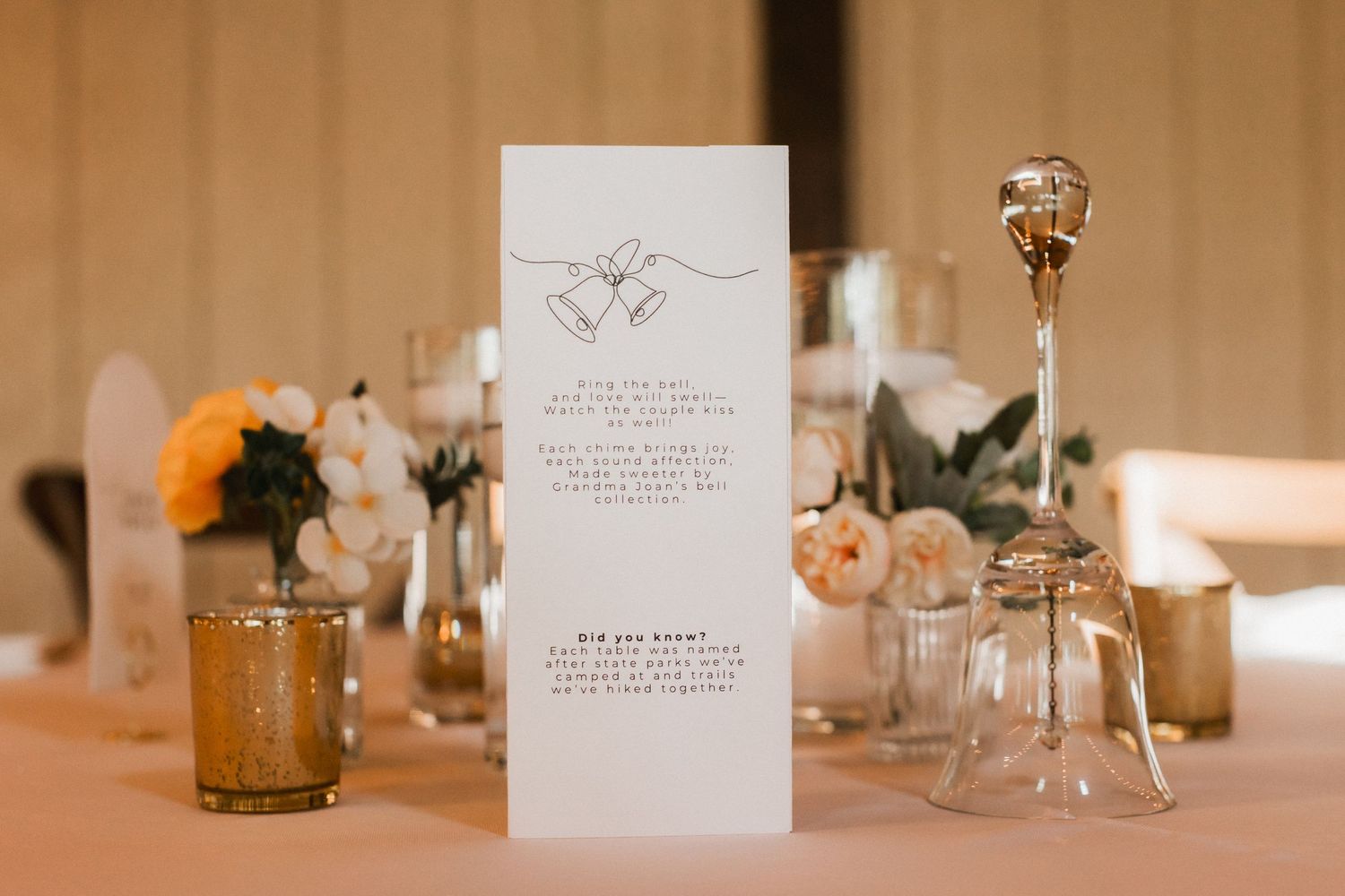 Elegant wedding menu card displayed with peach flowers and glass vases on a table setting.