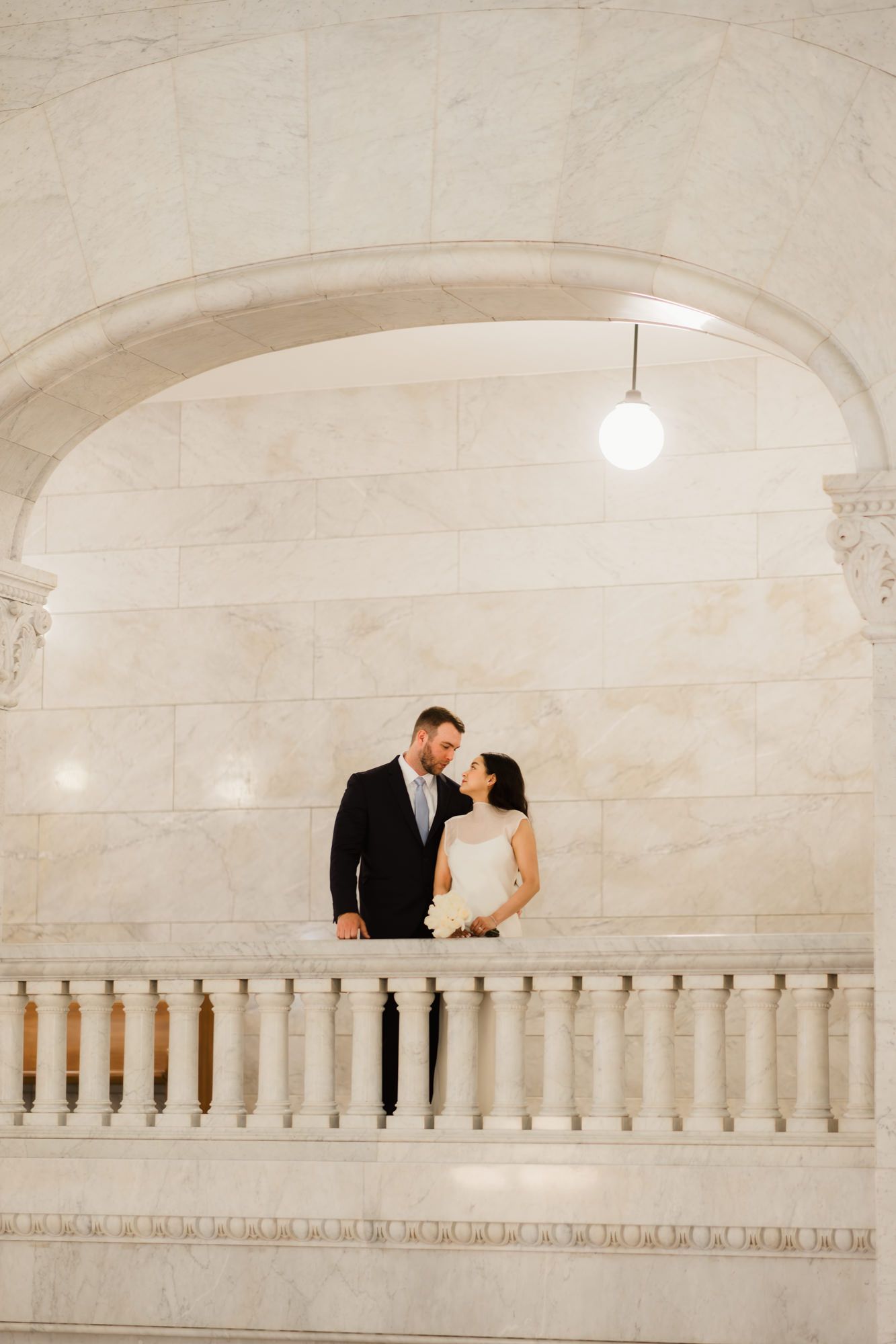 Bride and groom share a romantic moment under a marble arch at an elegant wedding venue.