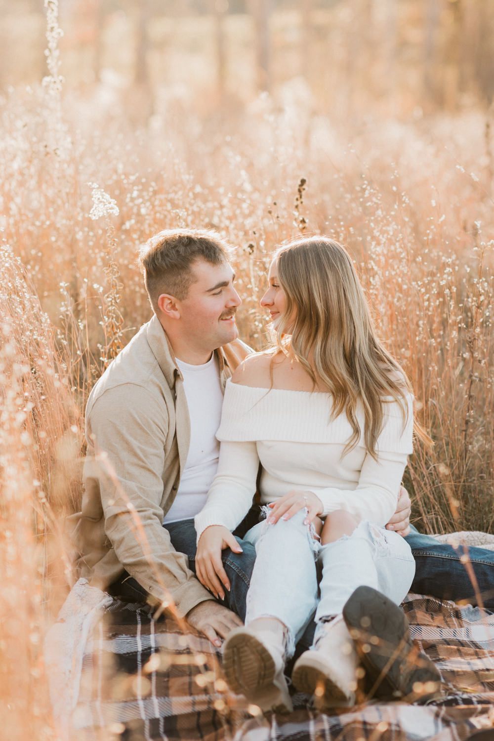 A couple sits on a plaid blanket sharing intimate moments in a golden field.