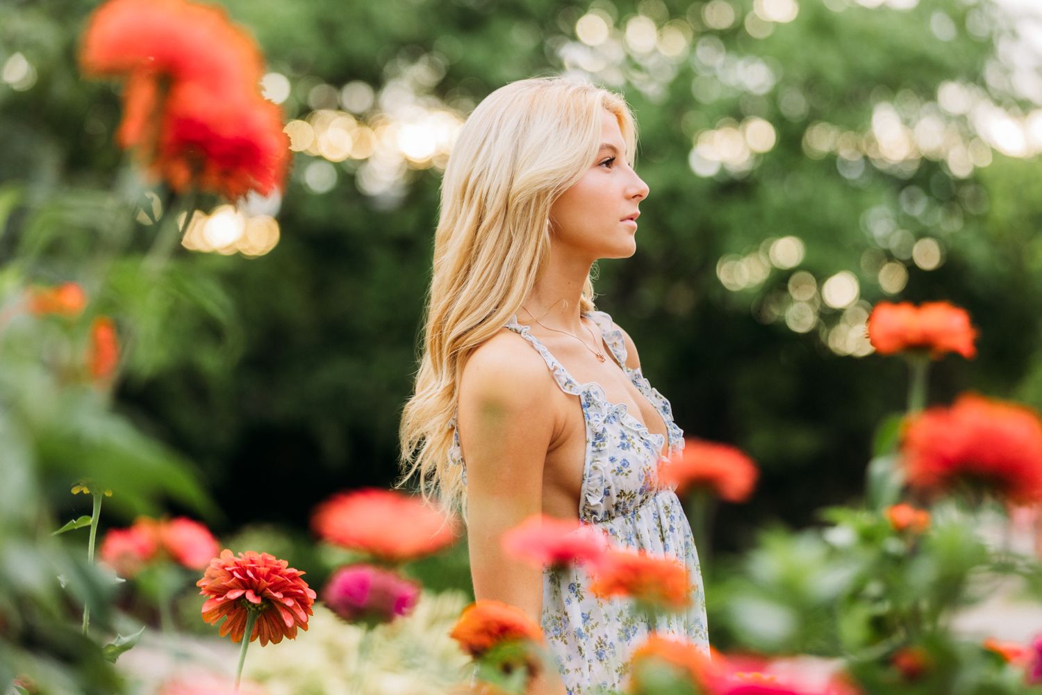 A woman in a floral dress stands among vibrant red zinnias in a summer garden.