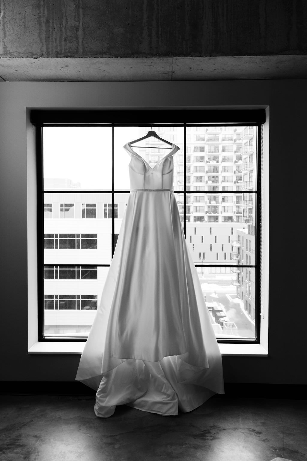 Wedding dress hanging in silhouette against industrial windows in black and white.