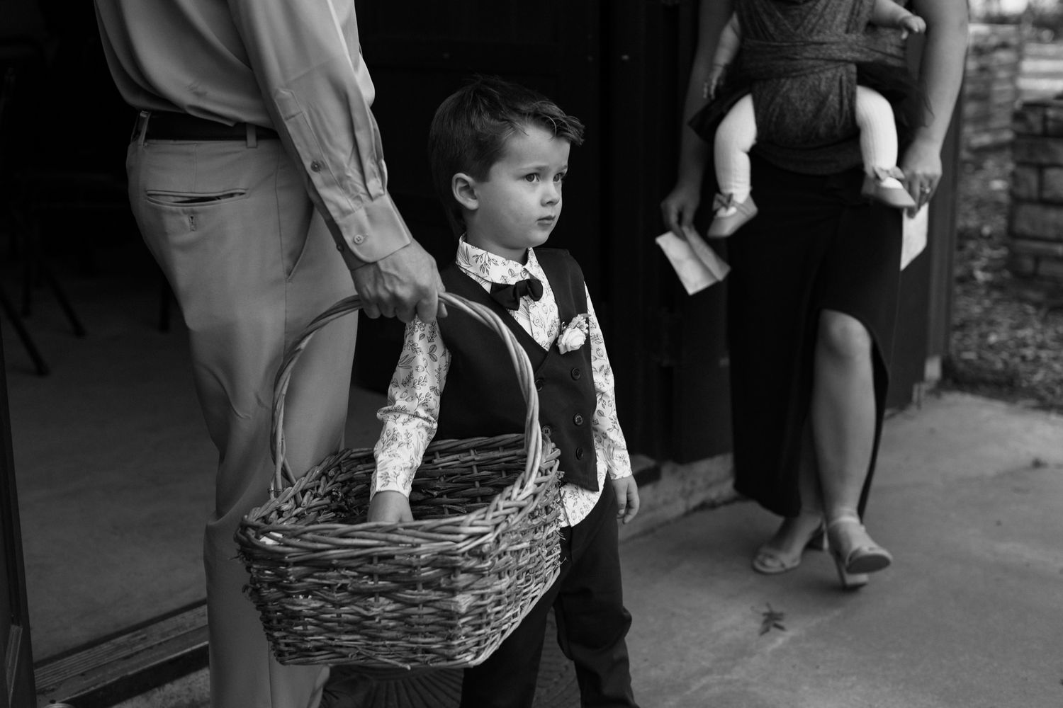 Young boy in formal attire holding a wicker basket at a wedding ceremony in black and white photo.
