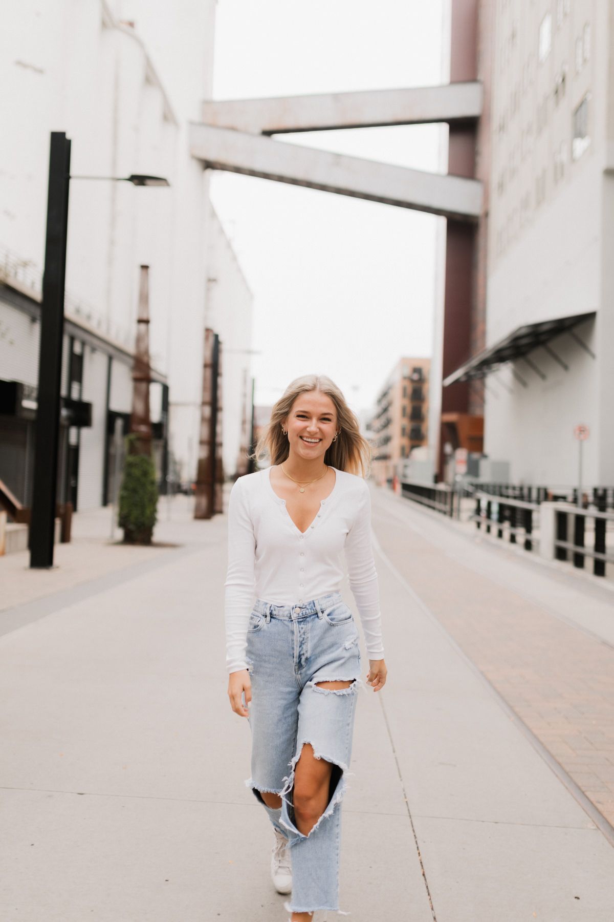 Young blonde woman walking confidently in ripped jeans and white top on an urban city street.