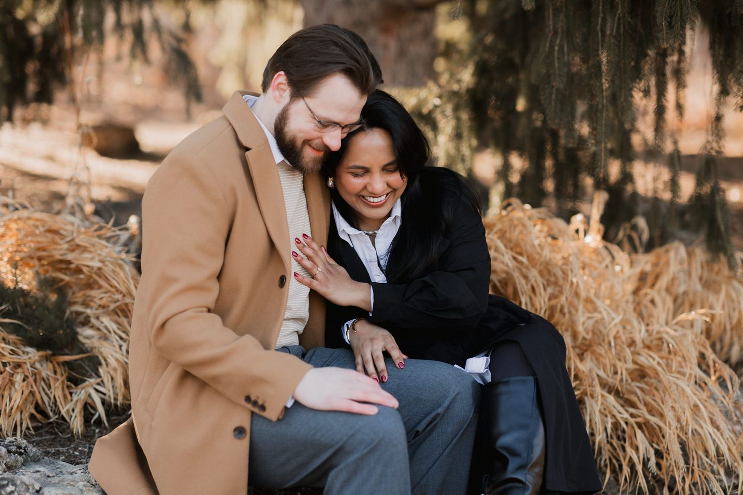 Happy couple sitting together outdoors in autumn, woman in black coat leaning on mans shoulder smiling.