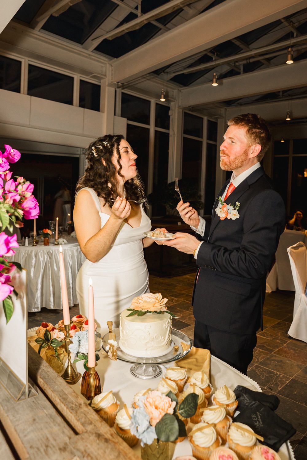 Wedding reception scene with cake cutting and florals in a glass-ceiling venue.