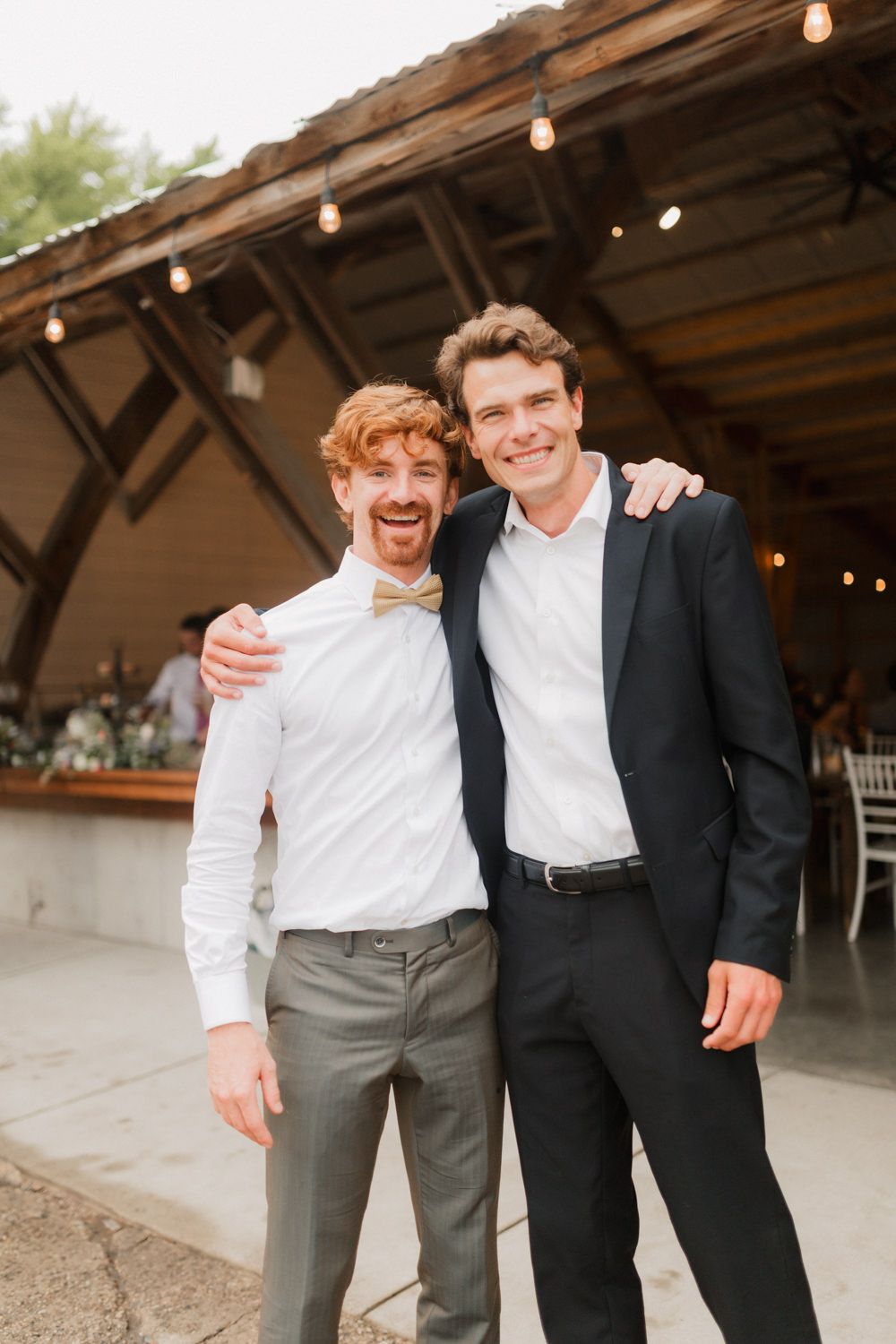 Wedding party members pose together in formal attire at a rustic outdoor venue.